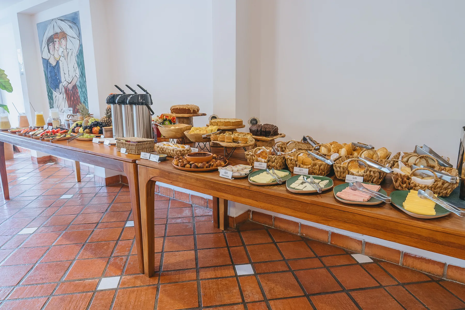 Mesa do café posta com pães, bolos e frutas