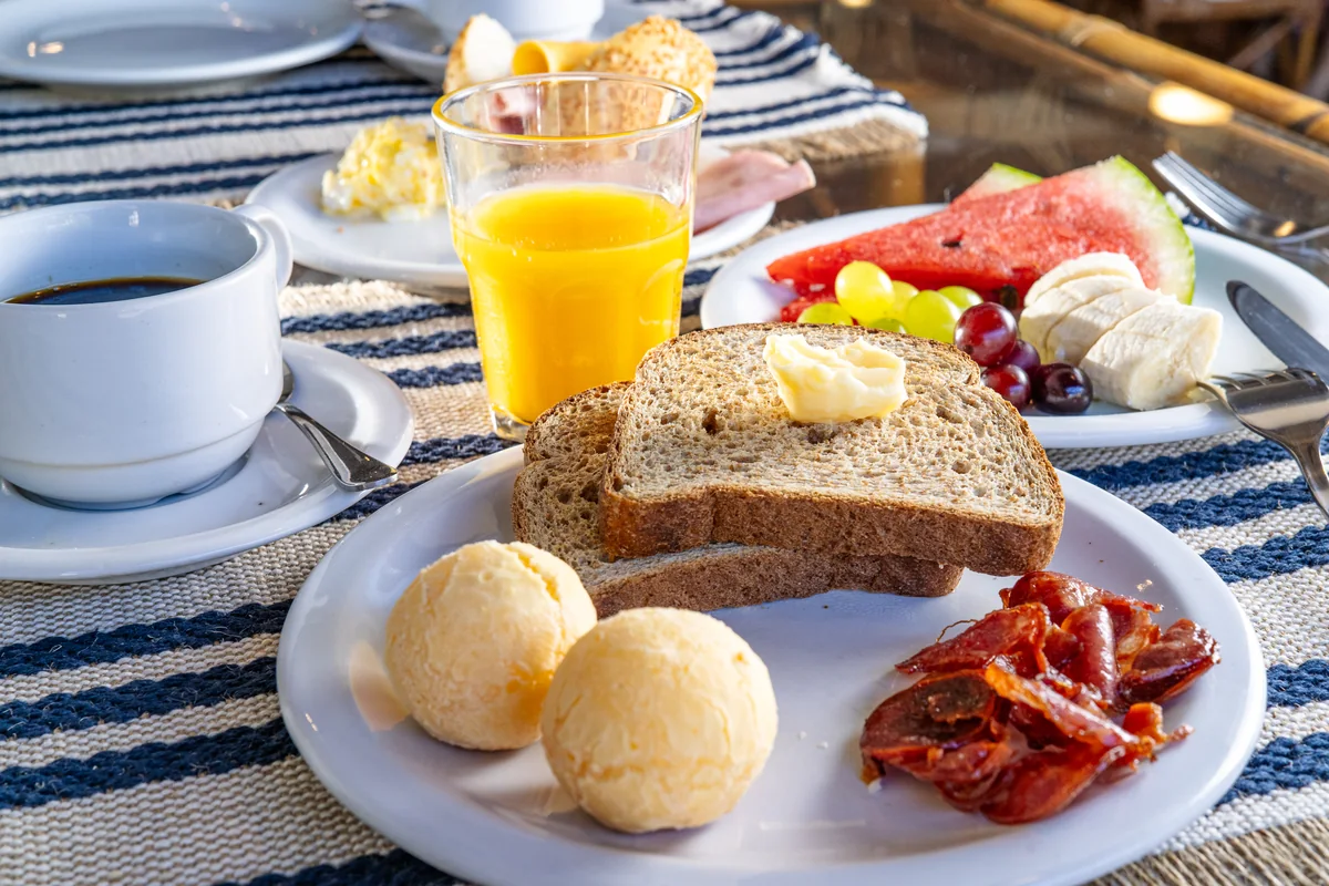 Mesa posta com café, suco, pão de queijo e frutas