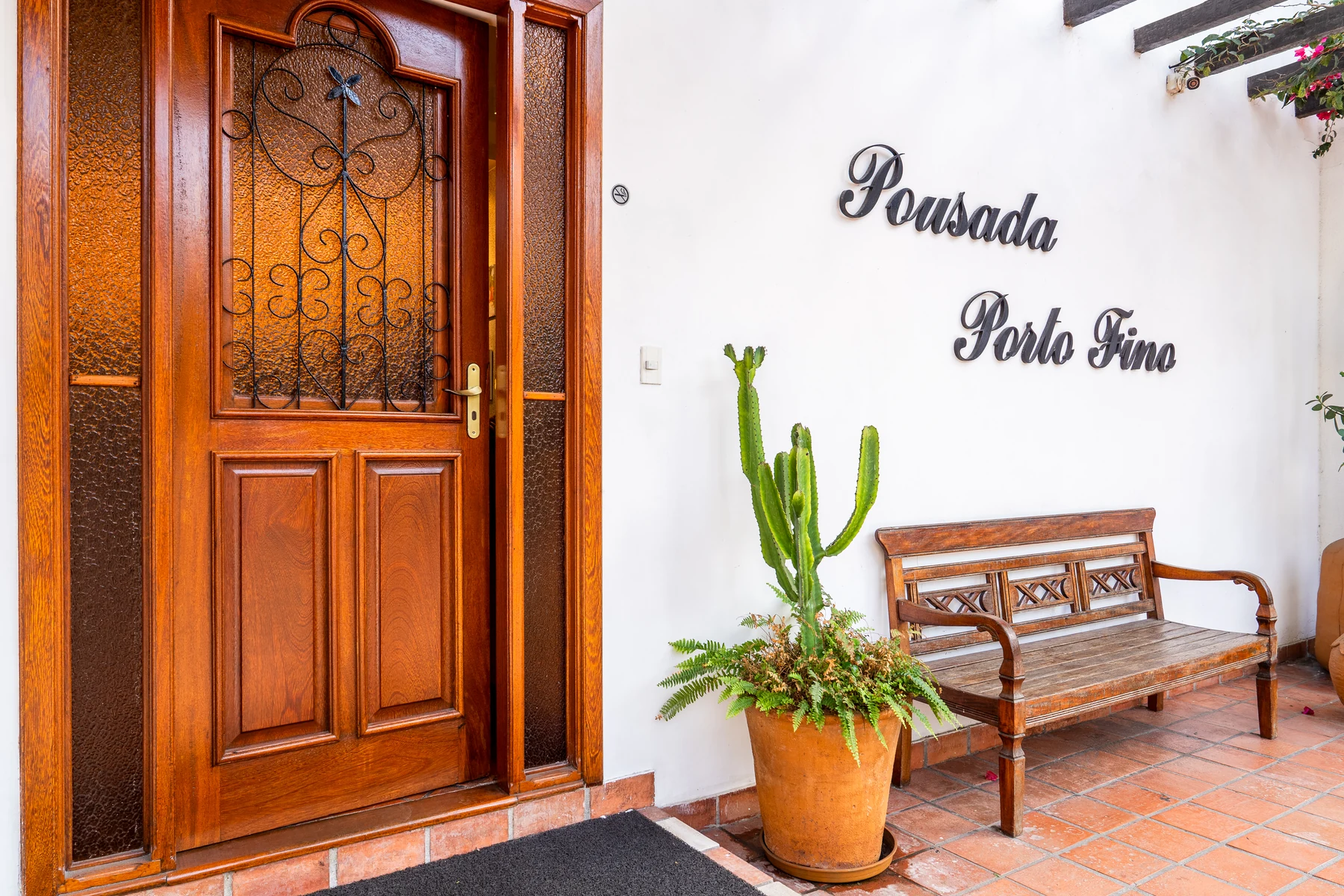 Entrada com o letreiro Pousada Porto Fino, banco de madeira e cactos