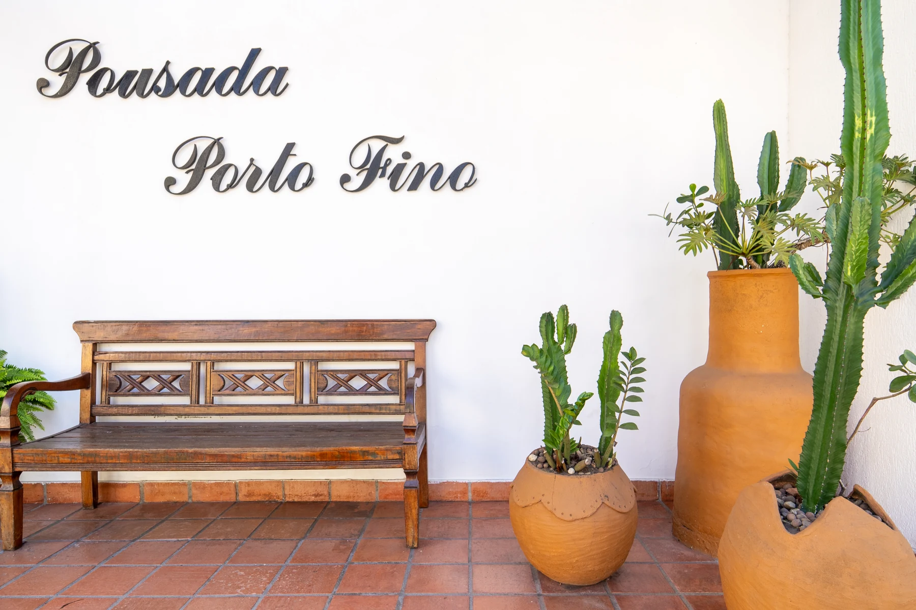 Letreiro Pousada Porto Fino na parede branca, com banco de madeira e cactos