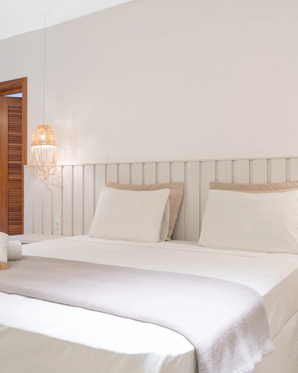 Cama king com cabeceira de ripas claras e luminárias de palha